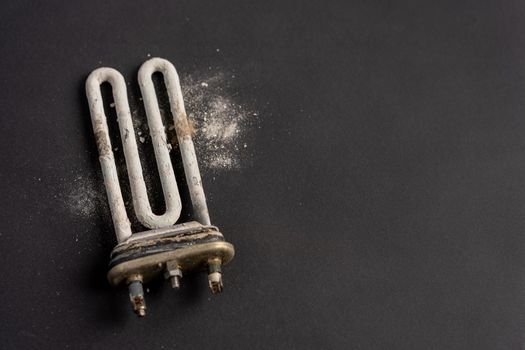 Damaged heating element of washing machine with scum and sediment on black background