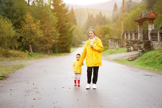 Rainy day Mother and little daughter walking after rain dressed yellow raincoat Happy family with one child. Positive emotions