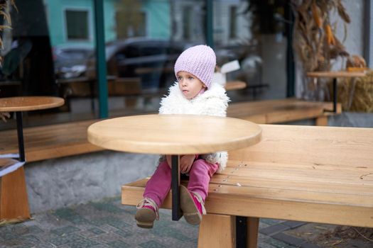 Unhappy little girl sitting outdoor cafe at table autumn season Caucasian female child losy in city sitting sad Lonely