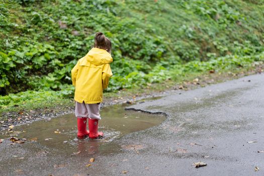 Playful girl wearing yellow raincoat while jumping in puddle during rainfall Happy childhood