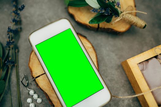 Smartphone with a blank screen lies on a beautiful wooden stand next to flowers and pearl earrings. High quality photo
