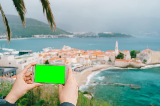 Smartphone in hands with a blank screen on the background of Budva. High quality photo
