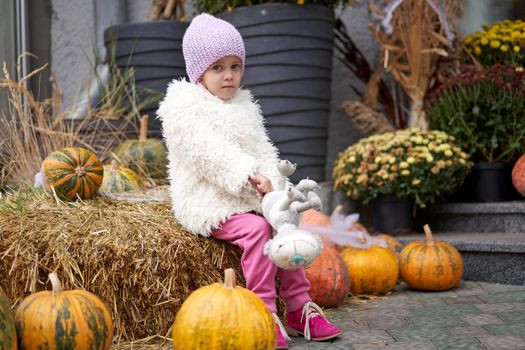 Unhappy little girl sitting outdoor Halloween pumpkin with toy cat autumn season Caucasian female child losy in city sitting sad Lonely