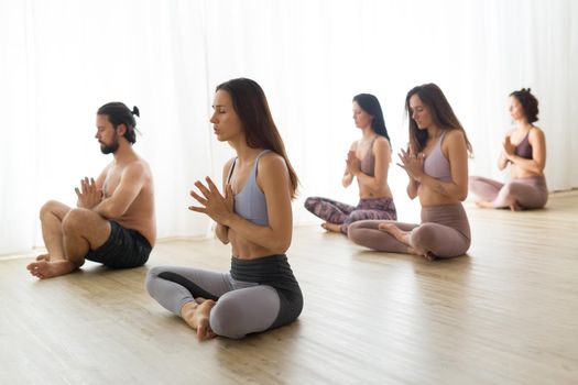 Group of young authentic sporty attractive people in yoga studio, practicing yoga lesson with instructor. Healthy active lifestyle, working out in gym.