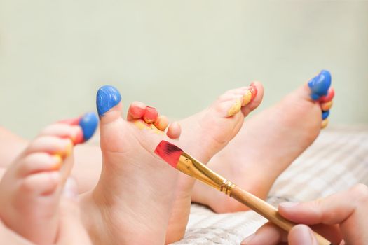 Baby art therapy child drawing on legs of kids colorful paints. Close up hand brush painting on feet children sensory play funny toes. Bare feet kids art development game drawing paint on legs child