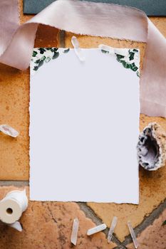 A blank white letterhead lies on a stone tile framed by a ribbon, a shell and a skein of thread. High quality photo