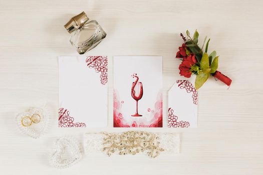 Wedding rings lie in a heart-shaped crystal box on the table. Nearby lies a small bouquet of roses, perfume and a watercolor painting with a picture glass of wine. High quality photo