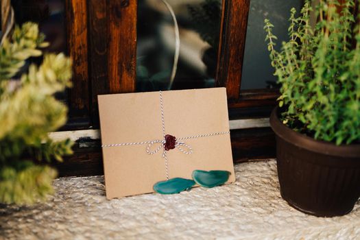 Brown envelope tied with a colorful string is on the white windowsill next to the flowerpots. High quality photo