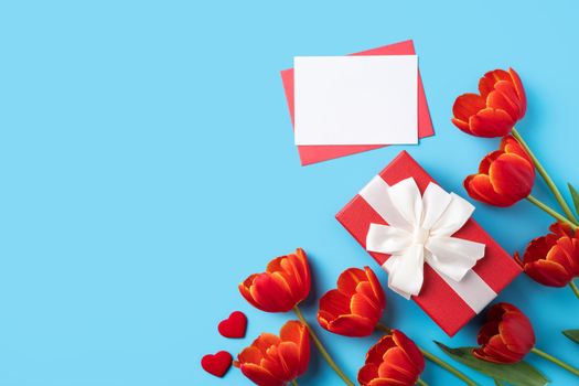 Design concept of Mother's day holiday greeting gift with red tulip bouquet and card on bright blue table background