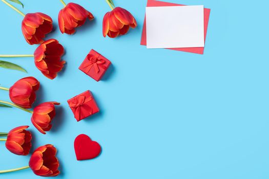 Design concept of Mother's day holiday greeting gift with red tulip bouquet and card on bright blue table background