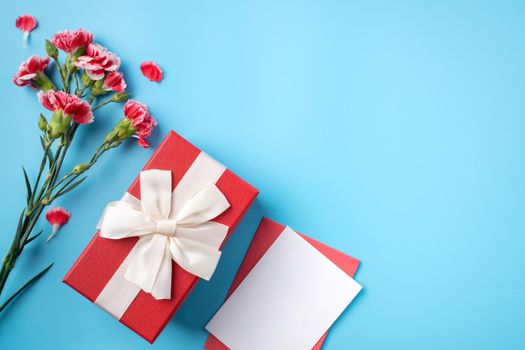 Mother's Day gift. Top view design concept of holiday greeting card with red carnation bouquet on bright blue table background