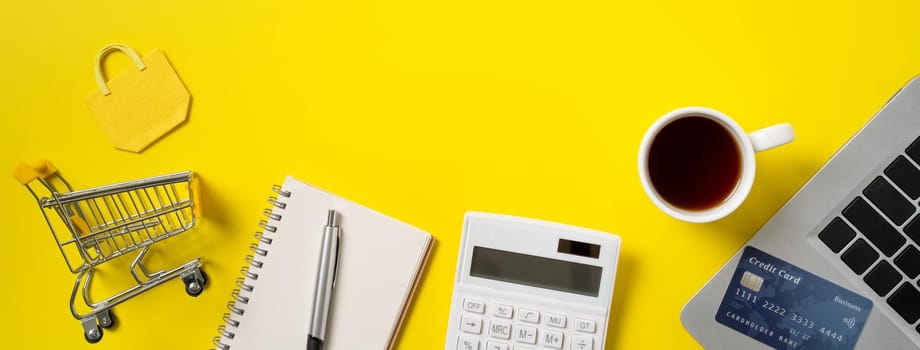 Online shopping concept. Top view of credit card purchase design concept with note, calculator and computer isolated on office yellow table background.