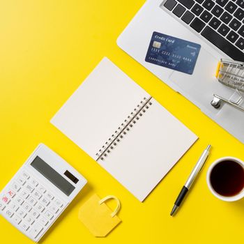 Online shopping concept. Top view of credit card purchase design concept with note, calculator and computer isolated on office yellow table background.