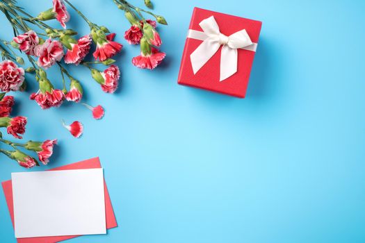 Mother's Day gift. Top view design concept of holiday greeting card with red carnation bouquet on bright blue table background