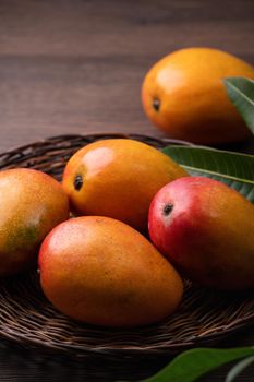 Mango. Close up of fresh ripe mango fruit on a bamboo sieve over dark wooden table background with green leaves.