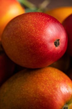 Mango. Close up of fresh ripe mango fruit on a bamboo sieve over dark wooden table background with green leaves.