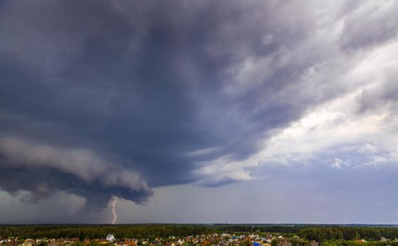 A violent thunderstorm with a hurricane and flashing lightning swept over the village. Dark clouds, rain and strong wind.