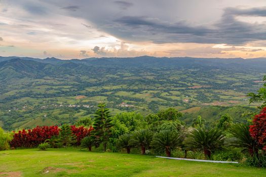 View from a large mountain to a valley with a lake in the Dominican Republic. Setting sun. Around greenery and red bushes