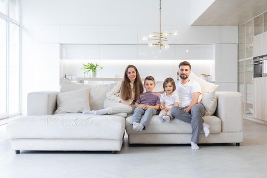 Family portrait of young parents with their two children at home, white modern desgin of living room