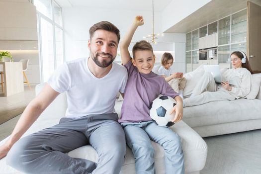 Family home life, father and son soccer fans cheering with football ball watching tv, daughter playing smartphone, mother listening music