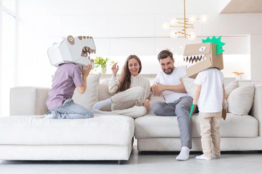 Happy family of parents and two children playing dinosaurs at home, children wearing handmade costume mask of cardboard