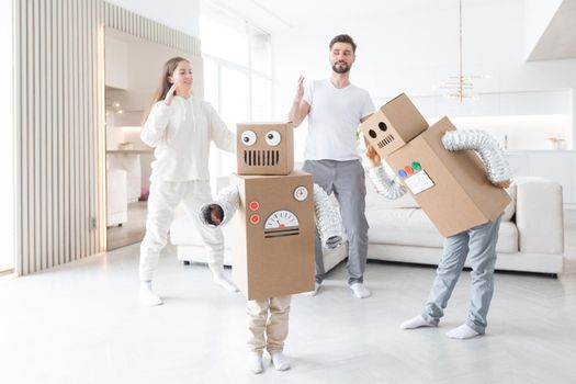 Happy family of parents and two children playing dancing like robots at home, children wearing handmade moving box costume of cardboard