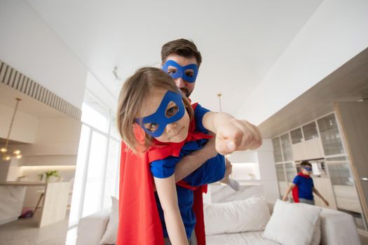 Father holding son flying in superhero costume at home