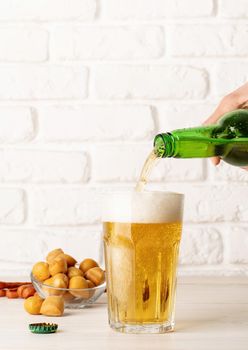 Jet of beer out of the bottle is poured into a beer glass, causing a lot of bubbles and foam, white brick wall background