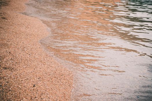 Sea beach in the tropics and the soft wave of the blue ocean. Summer gloomy day and sandy beach with stones background. The concept of summer vacation.