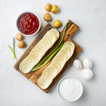 Crispy potato chips set, with dipping sauces tomato dip sour cream, on white stone surface, top view flat lay, square format