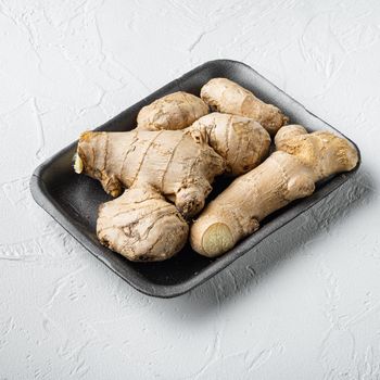 Trendy food whole ginger root set, in plastic market container, square format, on white stone background
