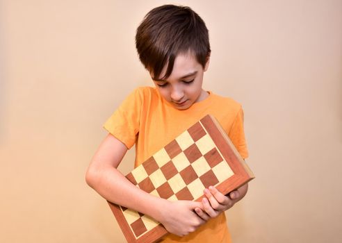 a boy holds a chessboard in his hands and looks at it.