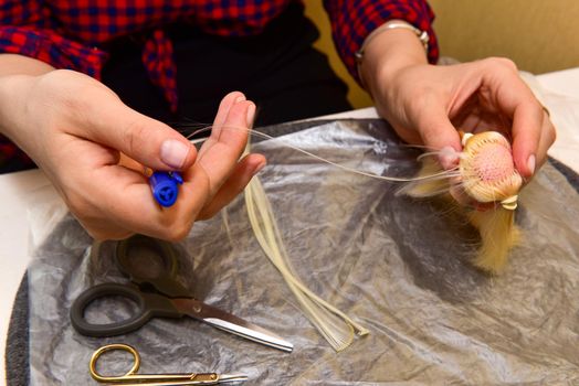 female hands and homemade tool on the table, how to make a hairstyle for a doll, hobby concept.