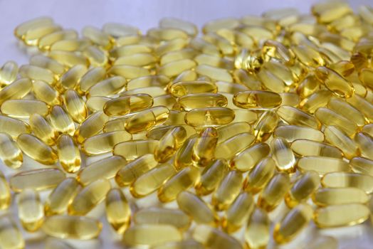 Bunch of omega 3 fish liver oil capsules in pile. Close up of big golden translucent pills texture. Healthy every day nutritional supplement. Top view.