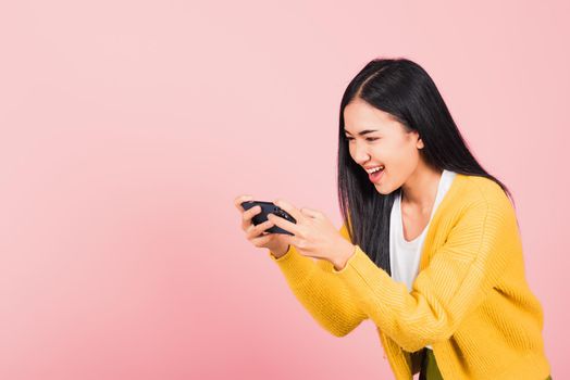 Happy Asian portrait beautiful cute young woman teen smiling excited   using mobile phone say yes! Studio shot isolated on pink background, Thai female surprised make winner gesture on smartphone