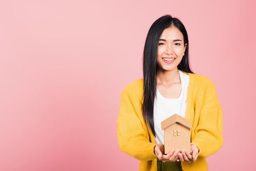 Happy Asian portrait beautiful cute young woman excited smiling holding house model on hand, studio shot isolated on pink background, broker female hold home real estate insurance and banking concept