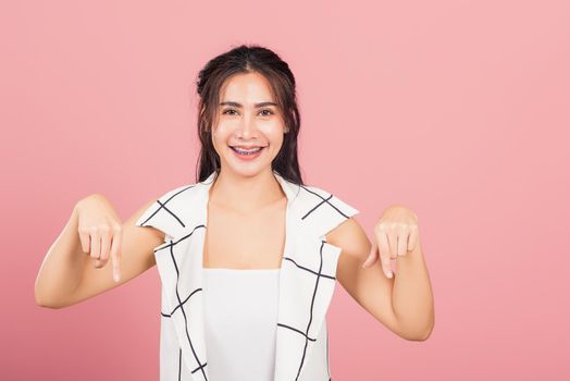 Portrait Asian beautiful young woman unhappy, negative gesture showing finger thumbs down or dislike sign, studio shot isolated on pink background, Thai female rejection unlike with copy space