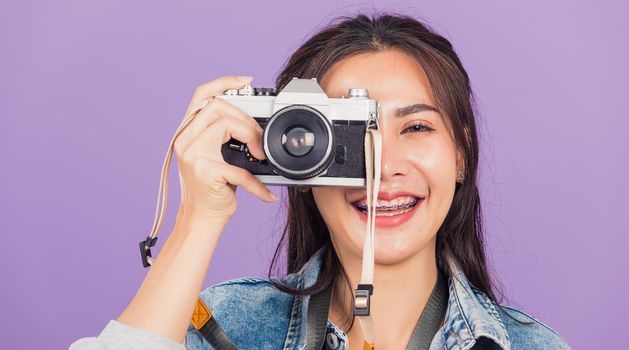 Portrait happy beautiful young woman smile excited wear denims photographer taking a picture and looking viewfinder on vintage photo camera ready to shoot, studio shot isolated on purple background