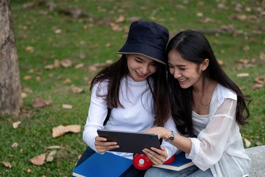 Two female university students outdoor study, using digital tablet together at the park in university.