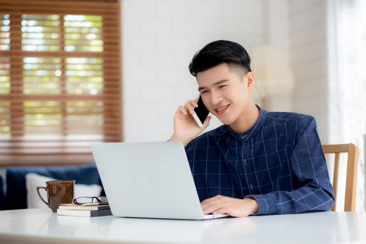 Young asian man talking phone and work from home with laptop computer, freelance using notebook to internet online and speak on smartphone, domestic life, business and communication concept.