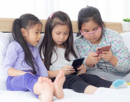 Happy asian little kid and friends playing smartphone on sofa at home, children using phone together on couch, girl watching smart phone for entertainment, lifestyle and communication concept.