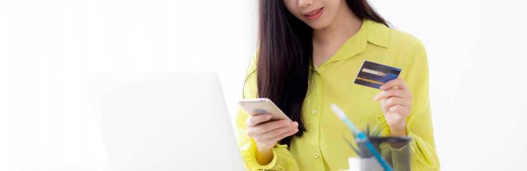 Young asian business woman using smart phone and holding credit card while online shopping and payment online with laptop computer on desk at home, female holding debit card, communication concept.