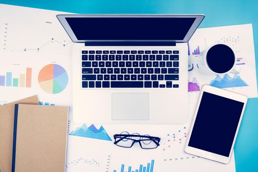 Laptop computer and documents report statistic financial with graph and chart and glasses and tablet, finance and invest, digital marketing and growth of revenue, business and communication concept.