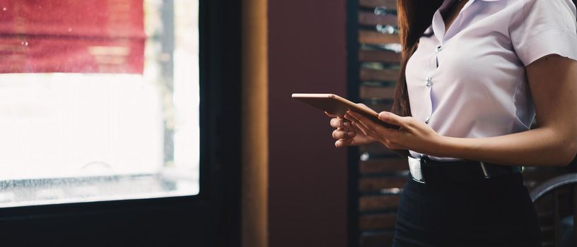 Cropped shot of female holding digital tablet touchscreen in hand, woman working on modern tech gadget in office with copy space.