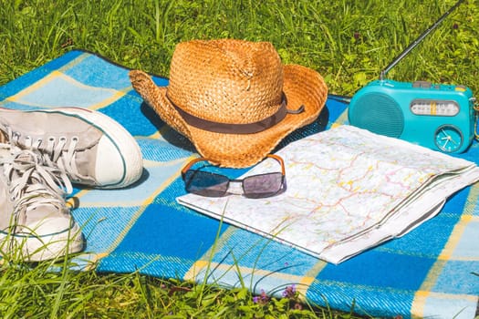 Picnic blanket with sneakers, straw hat, map and radio