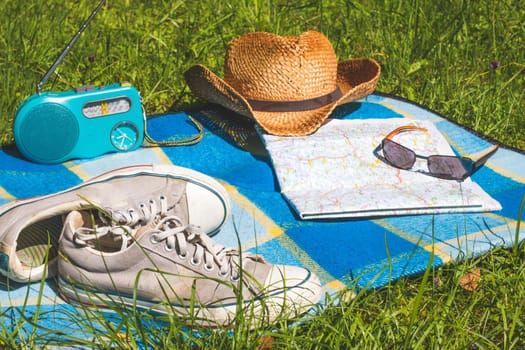 Picnic blanket with sneakers, straw hat, map and radio