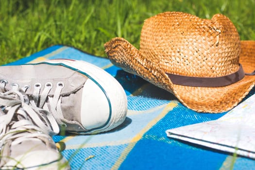 Picnic blanket with sneakers, map and straw hat