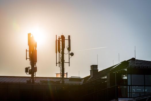 Silhouette of communication or cell tower on the rooftop of a building, evening sunshine