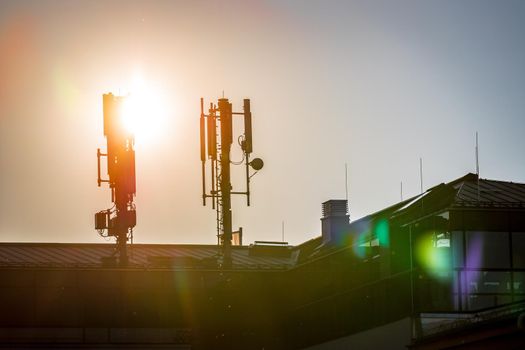 Silhouette of communication or cell tower on the rooftop of a building, evening sunshine