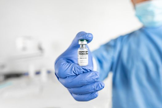 Selective focus hand close-up shot of senior doctor, nurse or healthcare worker in personal protective kit showing a vial of vaccine for treatment against Coronavirus or Covid-19 pandemic in hospital